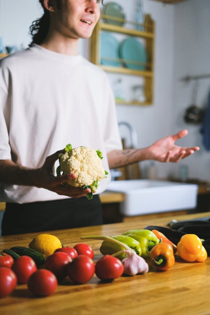 pexels photo 12673996 A man holds a cauliflower while preparing fresh vegetables in a modern kitchen.