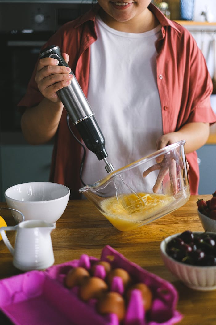 gallery-01 Person using a hand mixer to beat eggs in a modern kitchen setting.