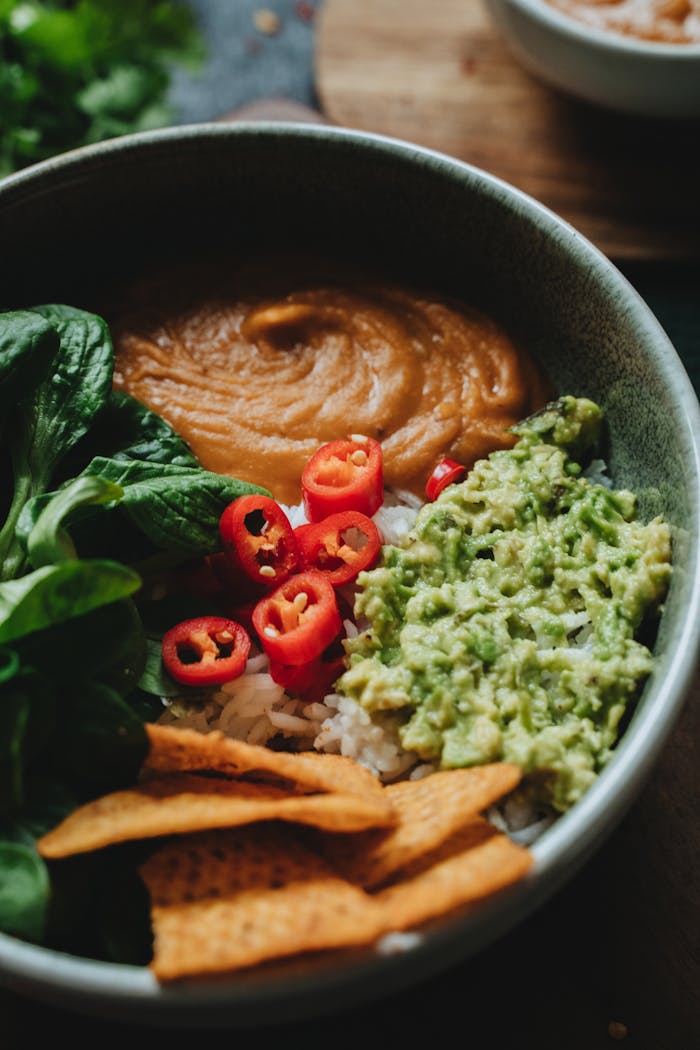 vision A vibrant vegan bowl featuring avocado, rice, chili peppers, and leafy greens, perfect for a healthy meal.